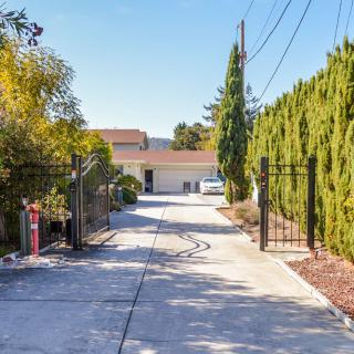 A long driveway leading to a house, bordered by trees and a gate.