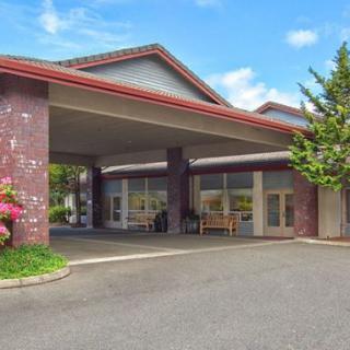A building with a covered entrance and driveway surrounded by greenery.