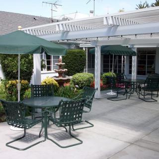An outdoor patio area with tables and chairs under umbrellas, surrounded by a garden and featuring a fountain.