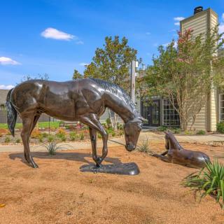 A bronze sculpture of a horse and a dog in an outdoor garden setting.