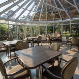 A spacious conservatory dining area with tables and chairs, surrounded by natural light.