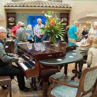 A musician plays the piano while people socialize at an indoor gathering.