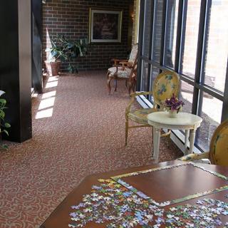 A cozy hallway with a puzzle on a table, flanked by elegant chairs and large windows letting in natural light.