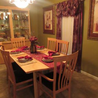 A warmly lit dining room with a wooden table set for dinner, surrounded by chairs and decorated with elegant place settings and a centerpiece.