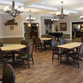 A spacious dining room with elegant chandeliers, wooden floors, and a grand piano.