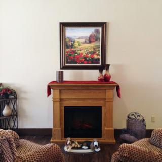 A cozy living room featuring a decorative fireplace, comfortable seating, and a beautiful landscape painting.