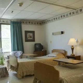 A hospital room with two beds, a television, and a window with curtains.