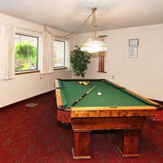 A cozy billiard room featuring a pool table with green felt and well-lit windows.