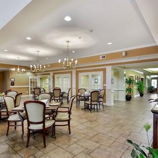 A spacious dining area with elegant chairs and tables, illuminated by chandeliers, featuring tiled flooring and decorative plants.