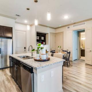 A modern kitchen with an island, featuring stainless steel appliances and wood flooring, adjacent to a cozy dining area.