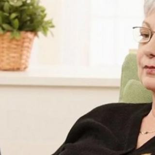 A woman with glasses relaxing at home near a potted plant.