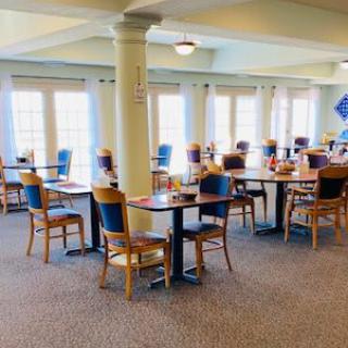 An empty dining area with neatly arranged tables and chairs, featuring large windows that brighten the space.