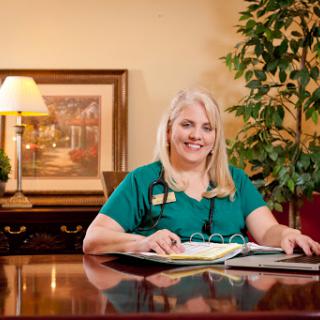 A cheerful woman in a green shirt sits at her desk, showcasing a welcoming office environment.