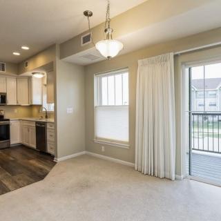 A modern apartment interior featuring a kitchen and dining area with natural light streaming through large windows.