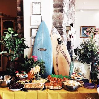 A vibrant tropical-themed buffet featuring a variety of dishes, accented by surfboards and lush greenery.