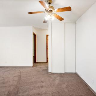 A spacious, empty bedroom featuring a ceiling fan and carpeted flooring.