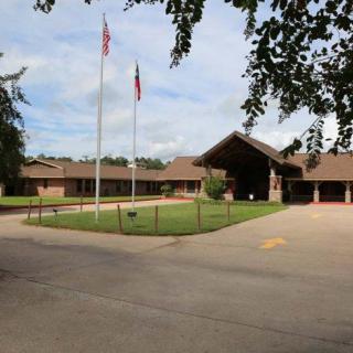 A single-story brick building with flags in front and a driveway, surrounded by greenery.
