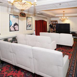 A spacious living room with white sofas, a chandelier, wall posters, and a large television.