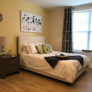 A cozy bedroom with a neatly made bed, decorative pillows, nightstand, and wall art.