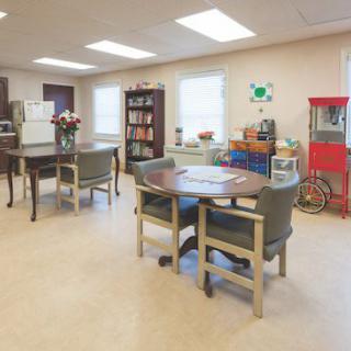 A well-lit room with tables, chairs, a bookshelf, and a popcorn machine.