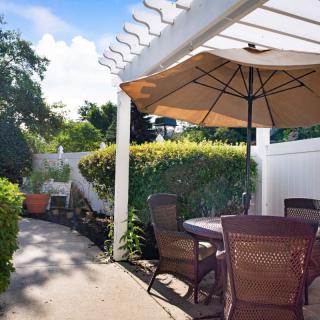 A sunny patio with outdoor furniture and a large umbrella, surrounded by lush greenery.