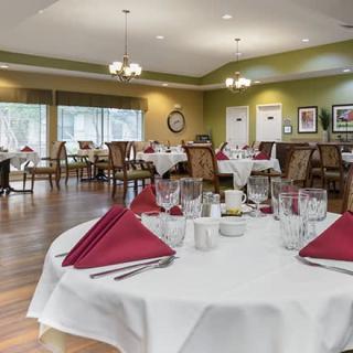 A spacious dining room with neatly set tables, featuring red napkins and glassware.