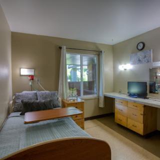 A well-equipped hospital room featuring a bed, desk, television, and natural light from the window.