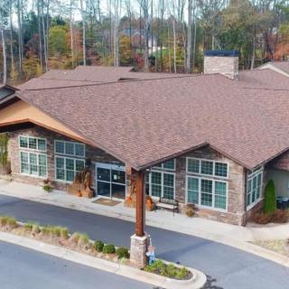 Aerial view of a building surrounded by trees, featuring a spacious parking lot and a prominent entrance.