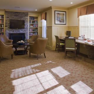 A cozy living room with comfortable seating, a fireplace, bookshelves, and natural light streaming in through the windows.