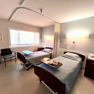 A well-lit hospital patient room featuring two beds and necessary furnishings.