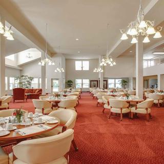 An elegant dining room with chandeliers, red carpet, and neatly arranged tables and chairs.