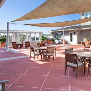 A sunny outdoor patio with tables and chairs, shaded by large sail-like canopies.