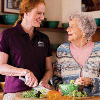 A caregiver assists an elderly woman with meal preparation in the kitchen.
