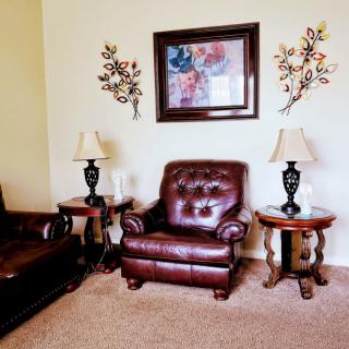 A cozy living room setup featuring a brown leather armchair, matching sofa, side tables with lamps, and decorative wall art.