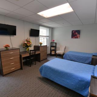 A neatly arranged bedroom with twin beds, decorated with blue bedspreads and equipped with essential furniture and a television.