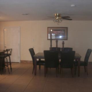 A spacious dining room with a large table and several chairs, featuring a ceiling fan and a wall painting.