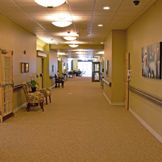 A well-lit corridor with chairs and artwork on the walls, likely in a hospital or nursing home.