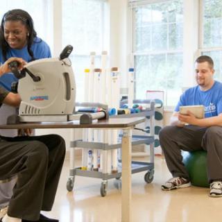 A therapist assists a patient using exercise equipment during a rehabilitation session.