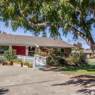 A charming residential house with a red door, surrounded by trees and landscaping.