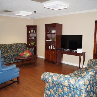 A cozy living room with floral-patterned sofas, a television, and wooden cabinets.