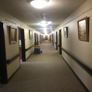 A well-lit hallway with paintings on the walls and carpeted flooring.