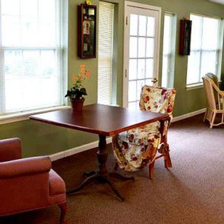 A cozy room with a wooden table, floral-patterned chairs, and large windows letting in natural light.