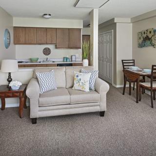 A cozy living room with a sofa and pillows, adjacent to a dining area and kitchen in an apartment setting.