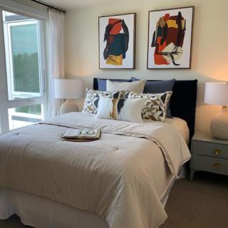 A modern bedroom with abstract artwork above the bed, featuring a cozy setup with pillows and bedside lamps.