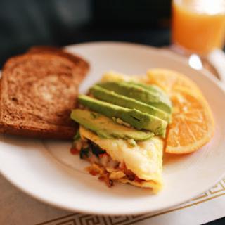 A delicious breakfast plate featuring a savory omelette topped with fresh avocado, served alongside toasted bread and orange slices.