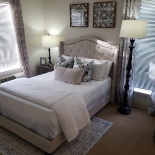 A cozy bedroom with a neatly made bed, two elegant lamps, and decorative wall art.