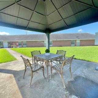 A cozy outdoor gazebo with a dining set, surrounded by lush green grass.