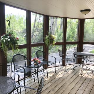 A cozy porch with tables and chairs, surrounded by windows and decorated with hanging plants.