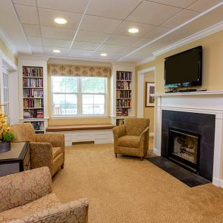 A cozy living room featuring a fireplace, television, armchairs, and bookshelves with a window seat.