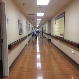 A long hospital corridor with wooden flooring and bright overhead lighting.
